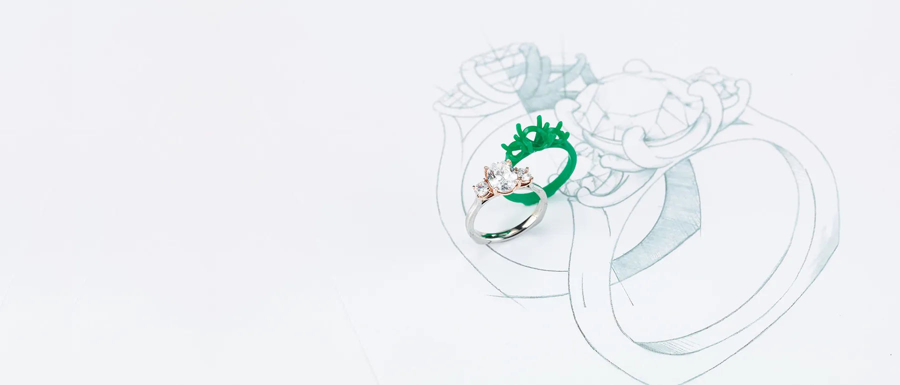 A finished three stone engagement ring beside its green wax model and pencil design sketch