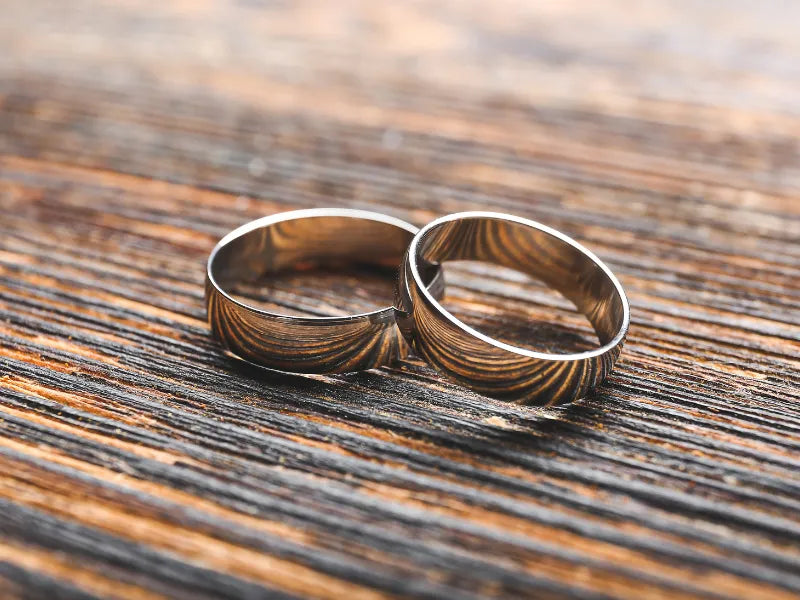 Two textured men's wedding bands resting on a wood grain surface